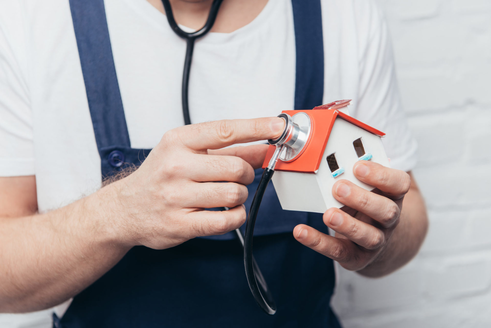 cropped shot of craftsman checking house figure by stethoscope, home inspection concept